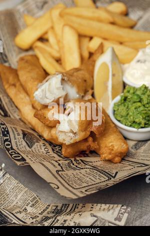 Britische traditionelle knusprige Fish and Chips mit pürierten Erbsen, Tatarsauce auf Zeitung Stockfoto