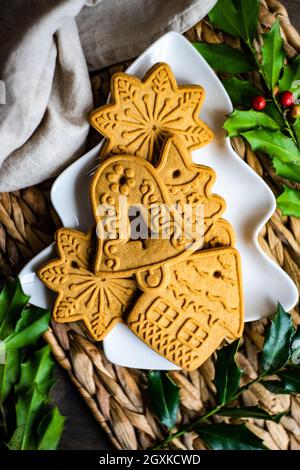 Weihnachts-Lebkuchenkekse auf einem baumförmigen Teller mit frischem Stechpalme Stockfoto