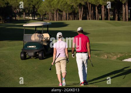 junges Paar zu Fuß zum nächsten Loch am Golfplatz. Mann Golf Tragetasche Stockfoto