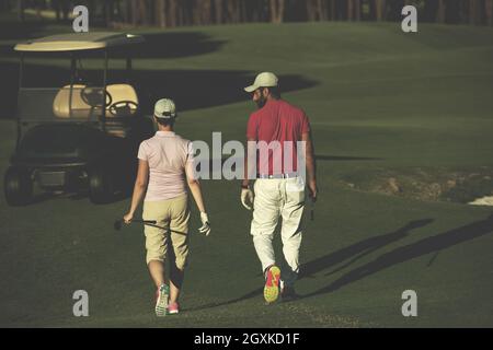 junges Paar zu Fuß zum nächsten Loch am Golfplatz. Mann Golf Tragetasche Stockfoto