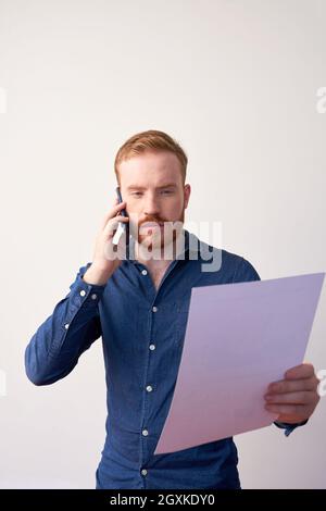 Beschäftigte junge kaukasische Managerin im legeren Hemd, die das Dokument analysiert, während sie ein Telefongespräch führt Stockfoto