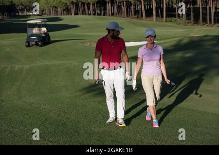 junges Paar zu Fuß zum nächsten Loch am Golfplatz. Mann Golf Tragetasche Stockfoto