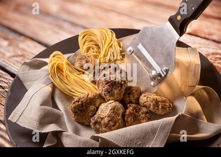 Weiße Alba-Trüffel auf Serviette mit rohem Ei-Tagliolini und Trüffelschneider aus Stahl auf Holzhintergrund Stockfoto