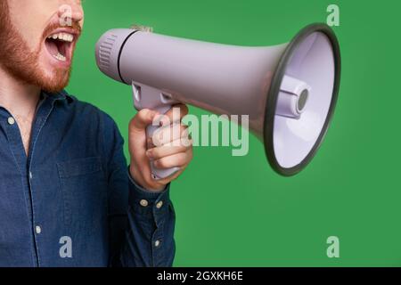 Nahaufnahme eines bärtigen Mannes, der vor grünem Hintergrund durch Lautsprecher schrie Stockfoto