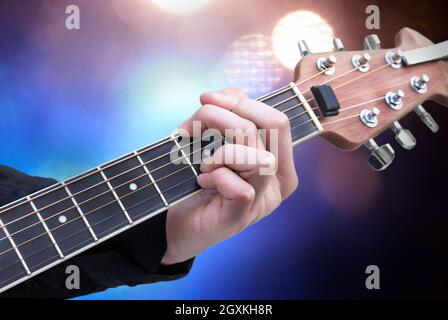 Eine kaukasische männliche Musikerhand schlägt einen Akkord an, während sie auf dem Hals seiner E-Gitarre mit Bühnenlicht im Hintergrund positioniert ist. Stockfoto