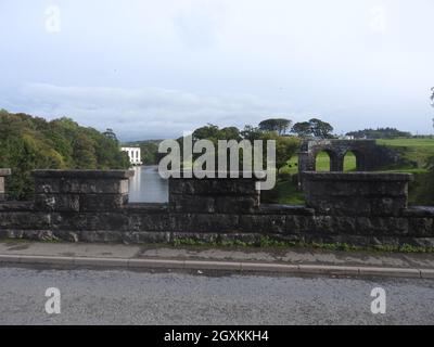 Tongland Bridge in der Nähe von Kirkcudbright, Dumfries & Galloway, Schottland. Es wurde von Thomas Telford (1757-1834) entworfen. In der Nähe befindet sich das Wasserkraftwerk Tongland (im Hintergrund gesehen). Die Brücke war zum Zeitpunkt ihrer Errichtung die erste große in Schottland. Sie wurde in den Jahren 1804-8 erbaut und ersetzte eine ältere Brücke stromaufwärts und war die erste Brücke, die anstelle eines massiven Mauerbogens gewichtssparende hohle Rippenspandrels hatte. Obwohl die Bauweise wunderschön ist, kann die ganze Pracht nur von Spaziergängern auf dem nahe gelegenen Fußweg am Fluss geschätzt werden, wie man sie von der Straße über nicht in ihrer Gesamtheit sehen kann. Stockfoto