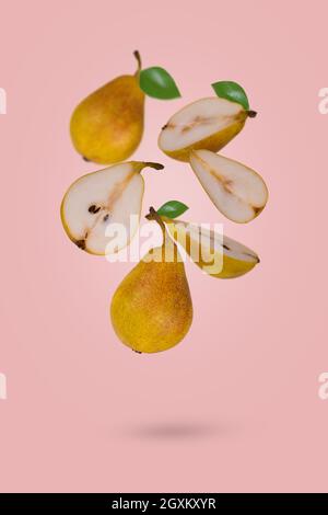 Kreatives Lebensmittelkonzept mit frisch reifen ganzen und geschnittenen Birnen, die in Luft fliegen, isoliert auf einem hellrosa Hintergrund. Vitamine, gesunde Ernährung Konzept. Stockfoto