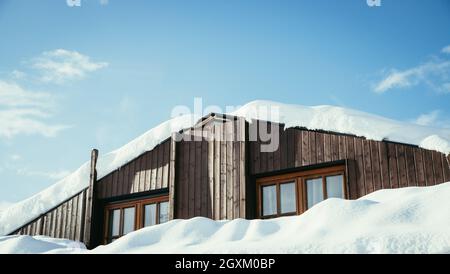 Modernes Holzhaus im Winter: Schnee auf dem Dach, blauer Himmel Stockfoto