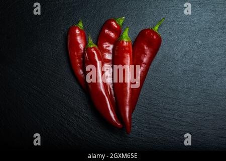 Fünf Chilischoten auf schwarzem Schieferbrett. Flach liegend. Stockfoto