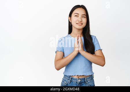 Nachdenkliche asiatische Frau hat einen Plan, stählerne Finger und lächelt mit einem selbstgefälligen Gesicht, schaut erfreut auf, interessante Idee, Intrigen vor weißem Hintergrund Stockfoto