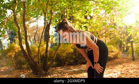 Porträt einer müden jungen Frau, die sich nach einem Rennen im Herbstpark ausruhte. Stockfoto