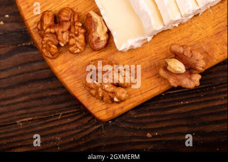 Geschnittene Kamembert- und Walnusskerne auf einem Holzschneidebrett, Nahaufnahme, selektiver Fokus Stockfoto