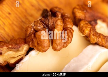 Geschnittene Kamembert- und Walnusskerne auf einem Holzschneidebrett, Nahaufnahme, selektiver Fokus Stockfoto