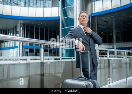 Ernsthafter Mann mit Koffer am Flughafen Stockfoto