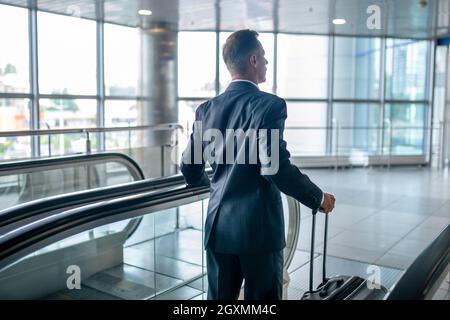 Rückansicht eines Mannes mit Koffer auf der Rolltreppe Stockfoto