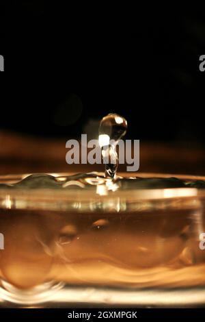 Wasser spritzt in einem Glas auf einem braunen, bernsteinfarbenen Hintergrund Stockfoto