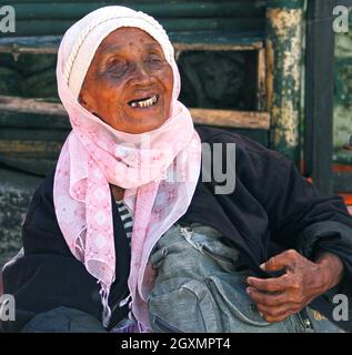 Eine alte blinde Frau, die in Bukittinggi, West-Sumatra, Indonesien, in einem rosa Hijab oder Tudung auf einer Straße sitzt. Stockfoto