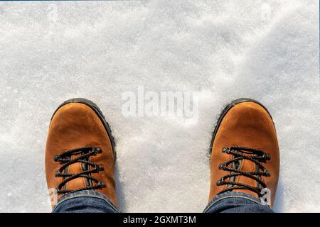 Nahaufnahme oben über Ansicht der männlichen Beine in Jeans und braunen Leder warme Stiefel isoliert auf weißen eisigen Schnee Oberfläche Hintergrund. Detail wasserdichte Schuhe Stockfoto