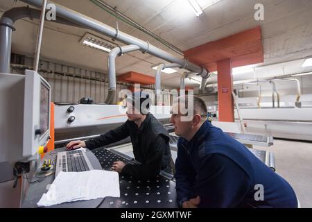 Zwei junge Tischler Berechnung und Programmierung einer CNC-Holzbearbeitung Maschine in der Werkstatt. Holz Arbeitnehmer vorbereiten - ein Programm für die CNC-Maschine Stockfoto