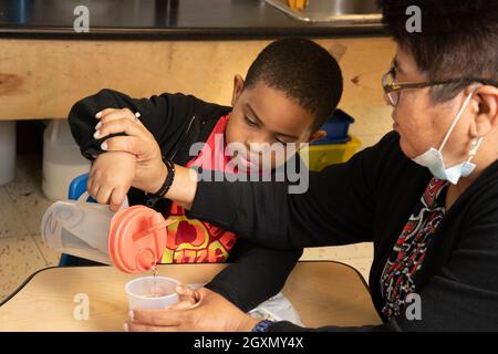 Bildung Vorschule 4-5-jährige Lehrerin unterstützt Jungen beim Eingießen von Wasser zur Essenszeit Stockfoto
