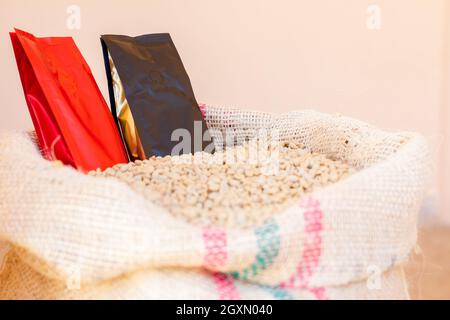 Beutel in fertigen Kaffeebohnen vergraben. Sack voll Kaffee. Verpackung in Rot, Schwarz und Gold. Industrialisierter oder verarbeiteter Kaffee auf Pergamentkaffee. Stockfoto