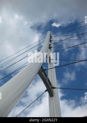 Aus der Wurmperspektive eine weiße dreieckige Brücke mit Hängekabeln, die einen blauen und wolkigen Himmel durchziehen Stockfoto