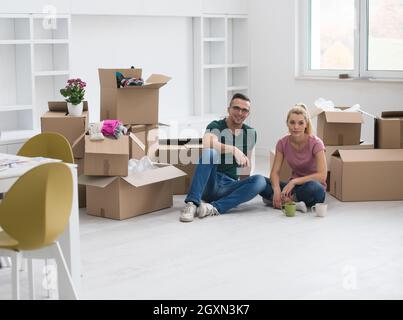 Entspannung im neuen Haus. Fröhliches junges Paar auf dem Boden sitzen und Kaffee trinken, während Kartons herumliegen Sie Stockfoto
