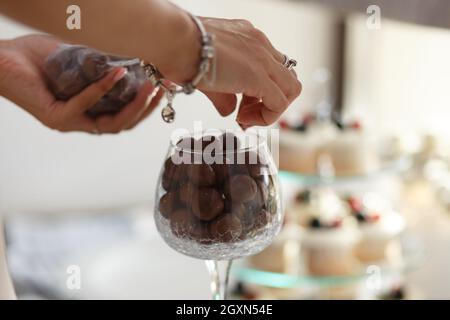 Weibliche Hände Servierteller mit runden Schokoladen-Bonbons in Weinglas auf festlichem Tisch Stockfoto