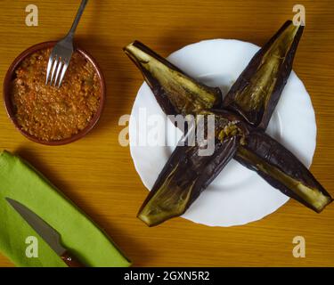 Leere Aubergine - Aubergine in einer Schale mit Bolognesse-Sauce in einer Tonschüssel, die mit silbernem Besteck und einer grünen Serviette verziert ist. Draufsicht Stockfoto