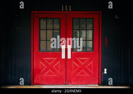 Rote Doppeltüren zum Gebäude 111 mit schwarzer Verkleidung Stockfoto