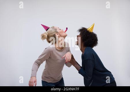 Menschen und Feier Konzept multiethnics lächelndes Mädchen in Partei Kappen weht zu pfeifen Stockfoto