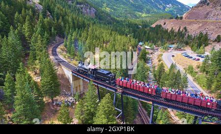 Alter Zug für Touristen, der über Brücke und Bach in den Bergen fährt Stockfoto