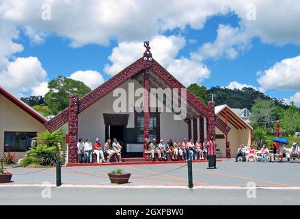 Touristen in Rotorua, Neuseeland, hören einem Führer zu, der über die Marae und das Maori-Dorf spricht, in dem sie sitzen. Indigener Tourismus und geothermischer Tourismus sind der Hauptanziehungspunkt für die Besucher dieses Lebensunterhaltungsgeldes, in dem Familien leben, arbeiten und die Umwelt respektieren, in der sie leben. Stockfoto