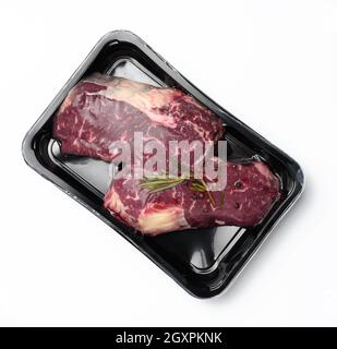 Zwei rohe Rindersteaks in einem Kunststoffbehälter mit Gewürzen und auf weißem Hintergrund gesaugt, Verpackung für die langfristige Lagerung, Draufsicht Stockfoto