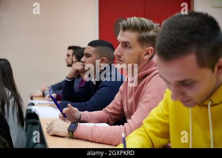 Im Klassenzimmer Multiethnische Studenten Hören Sie einem Dozenten zu und schreiben Sie in Notizbüchern. Intelligente junge Menschen studieren an der Hochschule. Stockfoto
