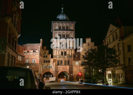 Lubeck Burgtor-Turm bei Nacht und eine leichte Spur eines durchfahrenden Fahrrads, historischer Backsteinbau der ehemaligen Stadtmauer und Häuser in der o Stockfoto