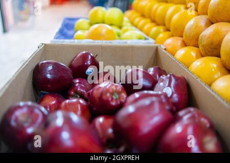 Nahaufnahme eines farbenfrohen Obststands mit frischen roten und gelben Äpfeln und Orangenhaufen. Saftig aussehende Früchte zum Verkauf auf Stand mit verschwommenem Hintergrund in Stockfoto