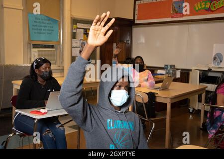 Bildung High School Klassenzimmer Szene, männliche Schüler heben Hand, um Frage zu beantworten, Schülerinnen hinter ihm, eine hebt ihre Hand Gesicht Masken Covid Stockfoto