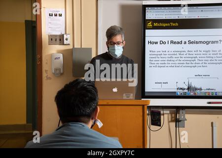 Bildung High School Klassenzimmer männlichen Lehrer präsentiert Unterricht auf Smart Board mit Laptop-Computer, wie männliche Schüler hört, trägt Gesichtsmaske Covid-19 Stockfoto