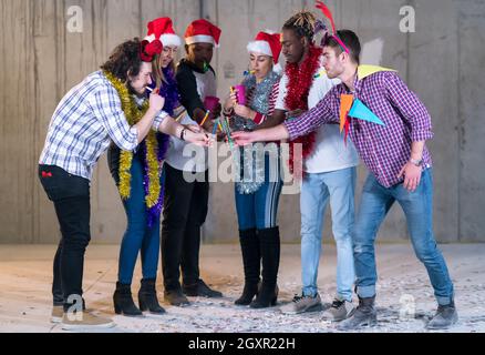 Multiethnische Gruppe junger happy and Business Leute Beleuchtung eine Wunderkerze und Spaß beim Silvester feiern in der betonwand an Stockfoto