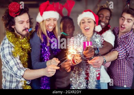 Multiethnische Gruppe junger happy and Business Leute Beleuchtung eine Wunderkerze und Spaß beim Silvester feiern in der betonwand an Stockfoto