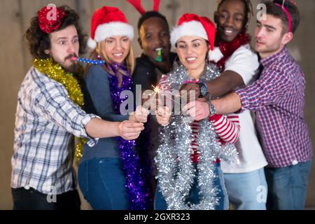 Multiethnische Gruppe junger happy and Business Leute Beleuchtung eine Wunderkerze und Spaß beim Silvester feiern in der betonwand an Stockfoto