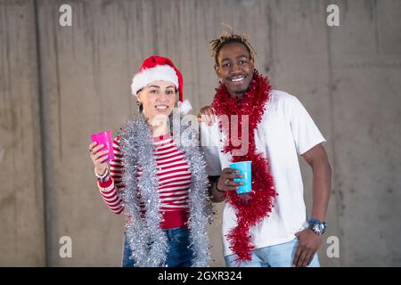 Junge casual multiethnischen Geschäft paar Spaß beim feiern das neue Jahr Partei in unfertigen startup Office mit einer grauen Wand hinter Ihnen Stockfoto