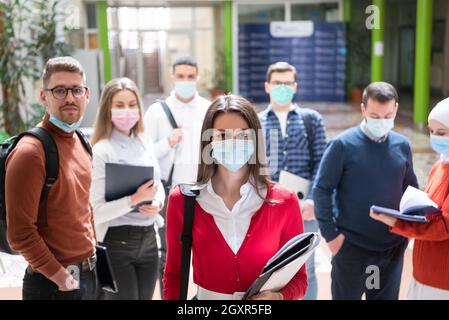 Multiethnische Studentengruppe, die in der Bildung auf einem Universitätskoridor mit einer schützenden Gesichtsmaske in einem neuen, normalen koronavirus-pandemischen Lebensstil läuft Stockfoto