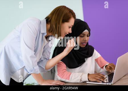 eine afromuslimische Frau mit einem Hijab sitzt lächelnd in ihrem Heimbüro und nutzt einen Laptop für Online-Meetings Stockfoto