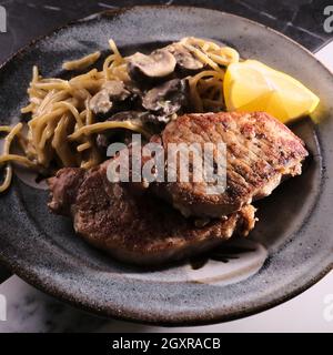 Gebratene Schweinekoteletts mit Honig-Senf-Pilzsoße und Pasta Stockfoto