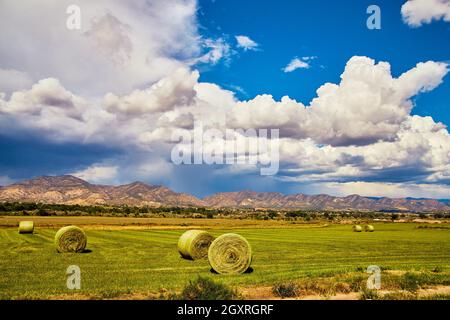 Heuballen im grünen Feld mit Bergen und Sturmwolken im Hintergrund Stockfoto