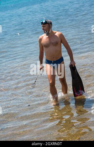 Junge lächelnde Fischer mit Ausrüstung im flachen Wasser des Meeres während der Vorbereitung für die Unterwasserjagd aktiv Urlaub Konzept Stockfoto