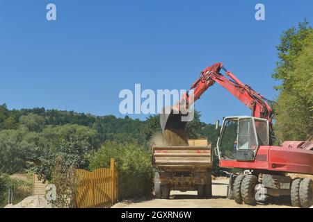 Foto eines Flurförderbaggers, der Erde bewegt und in einen LKW entladen wird Stockfoto