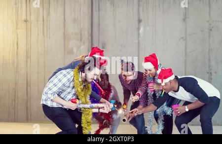 Multiethnische Gruppe junger happy and Business Leute Beleuchtung eine Wunderkerze und Spaß beim Silvester feiern in der betonwand an Stockfoto